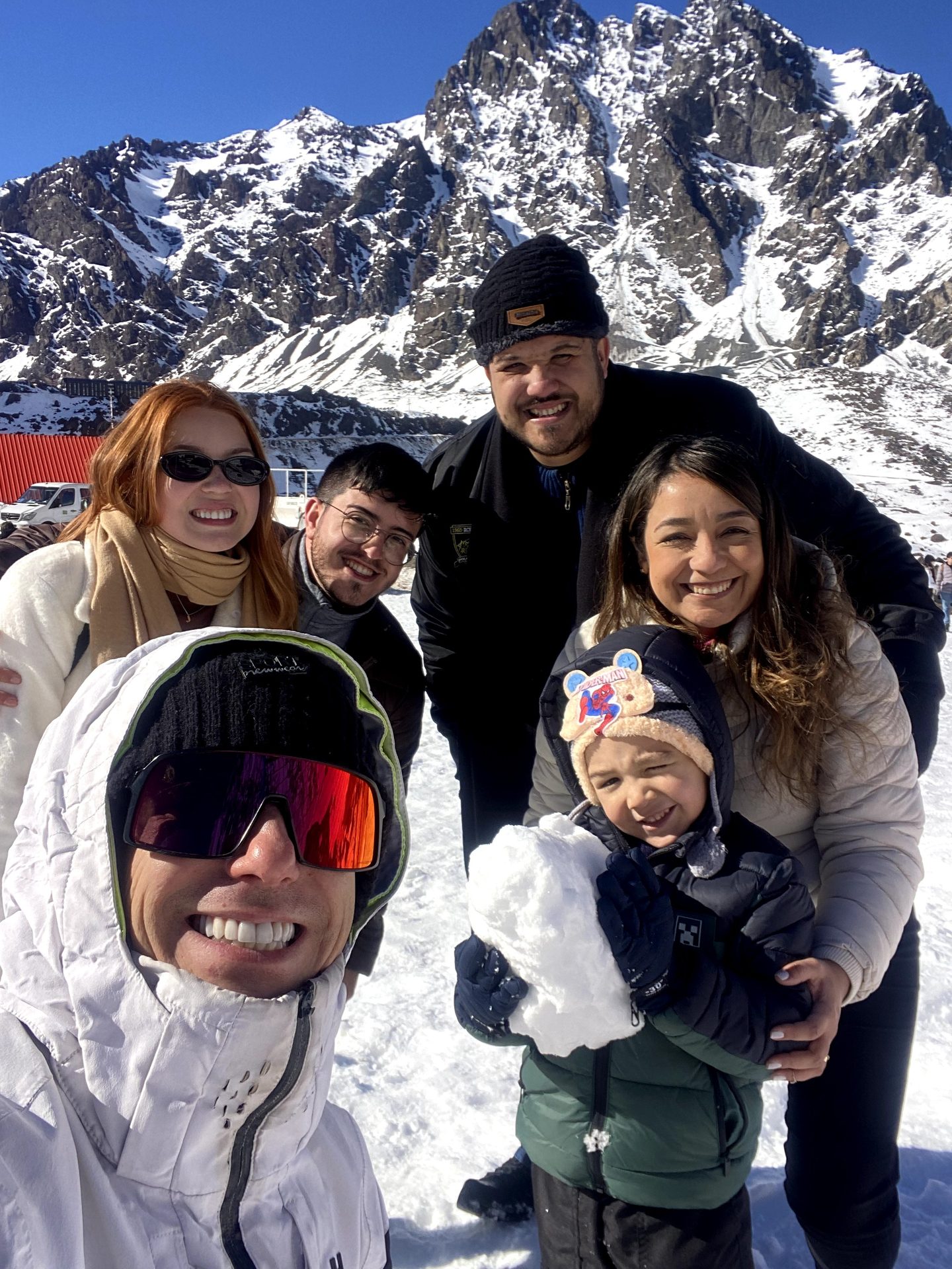 Família brasileira com criança nos braços, cordilheira nevada ao fundo